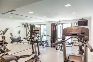 Un gimnasio con diferentes máquinas de ejercicio, un espejo grande y un televisor en la pared.