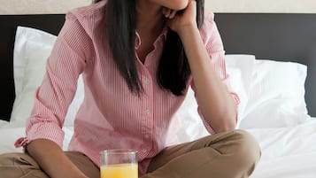 Una persona sentada en una cama con un plato de comida y un vaso de jugo de naranja.