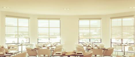 Un comedor amplio con varias mesas y sillas, ventanas grandes con vistas al exterior y un interior luminoso y bien iluminado.