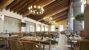 A spacious dining area with wooden tables and chairs, chandeliers, and a large potted plant. - Fiesta Inn Toluca Tollocan (Toluca)