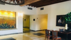 A lobby with a large painting of a landscape, a reception desk with chairs, and a tiled floor. - Fiesta Inn Toluca Tollocan (Toluca)
