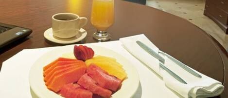 A breakfast plate with salmon, strawberries, and orange slices, a cup of coffee, and a glass of orange juice on a table.