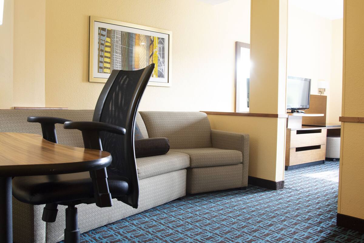 A hotel room with a sofa, a dining table, a TV, and a patterned carpet.