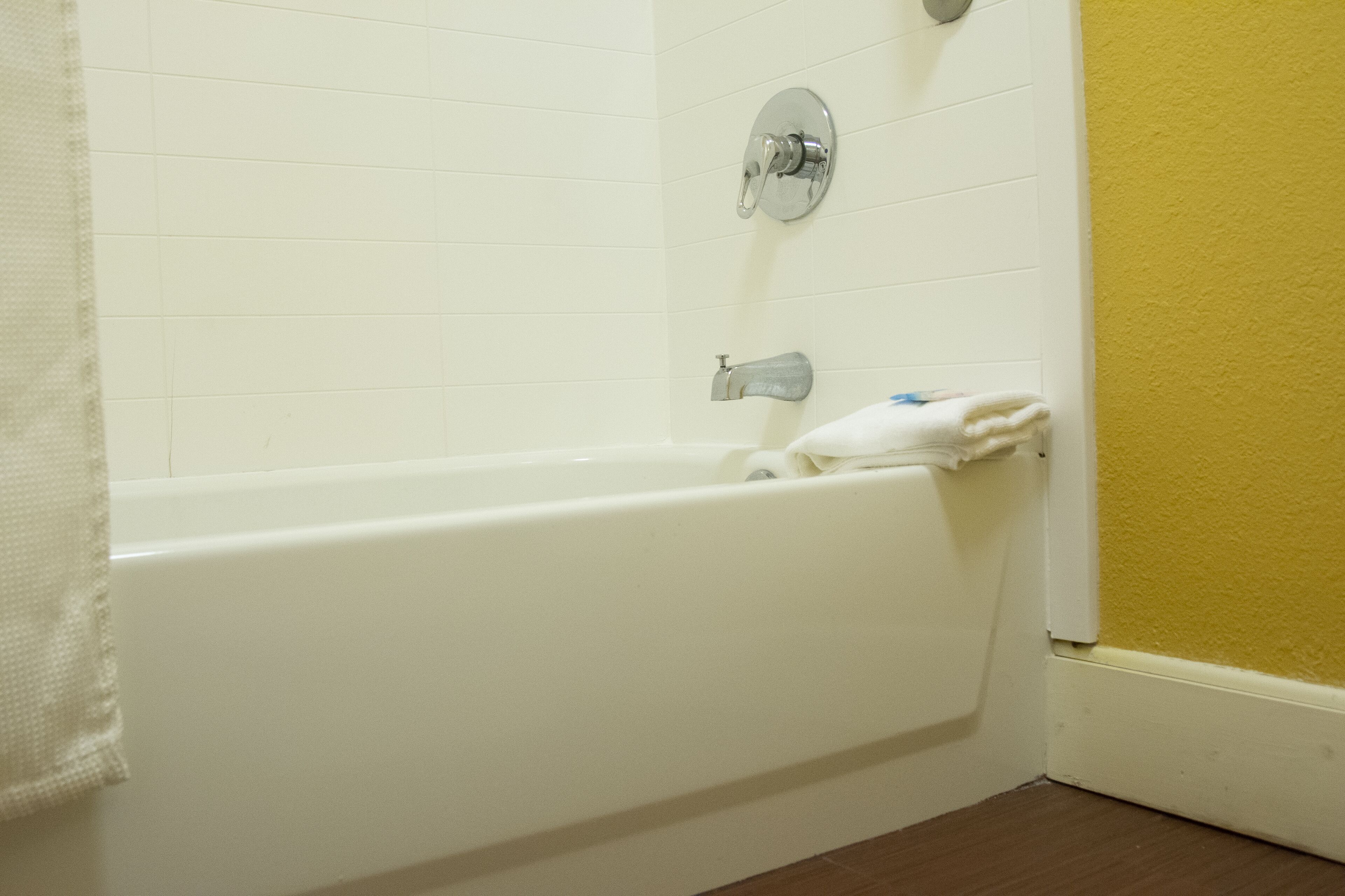 Eine weiße Badewanne mit Handtuch, Chromarmaturen und einer gelben Wand.