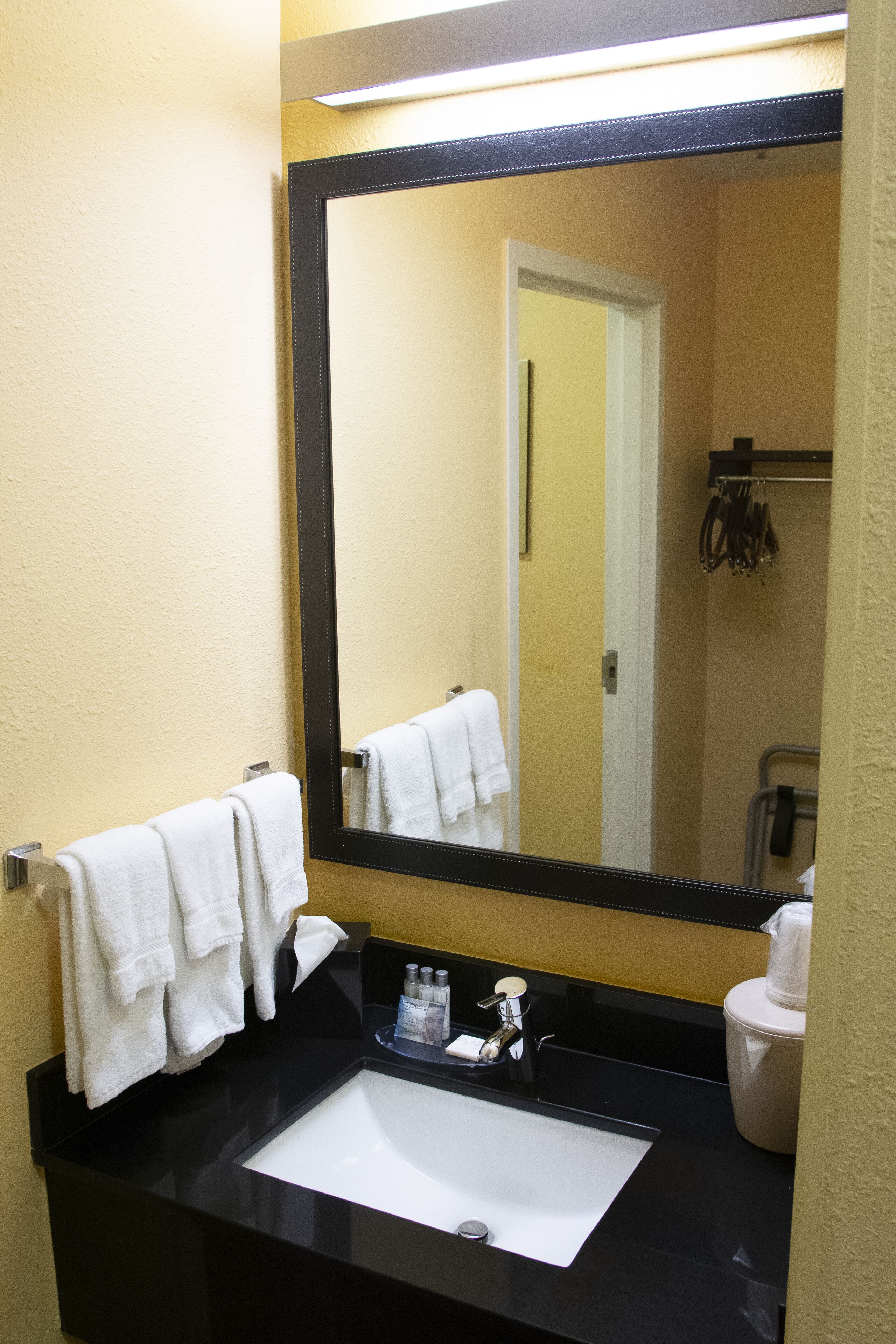 Un baño con lavabo negro, toalla blanca y un espejo grande.