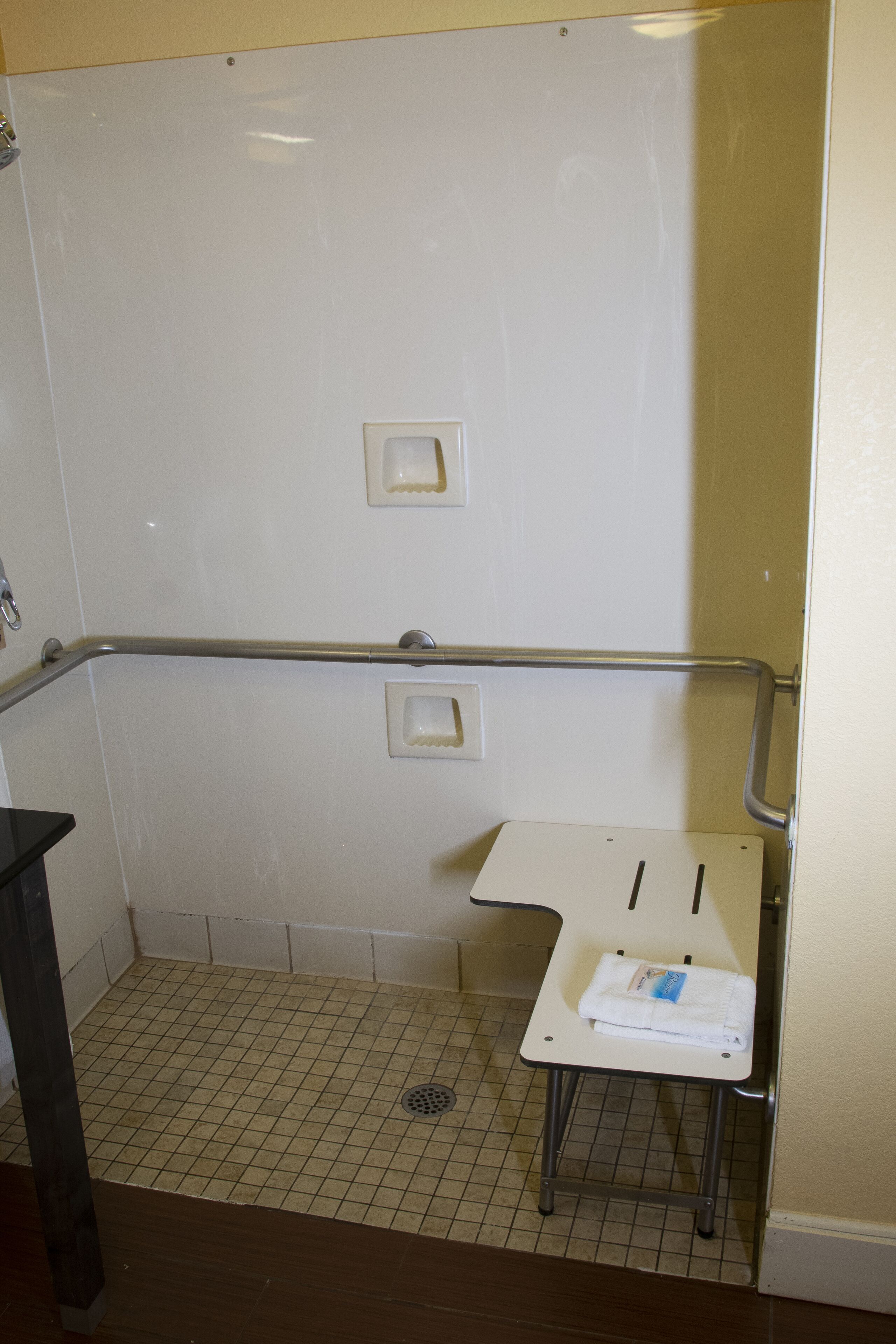 A bathroom with a white tiled floor, a white sink with a towel, and a metal grab bar.
