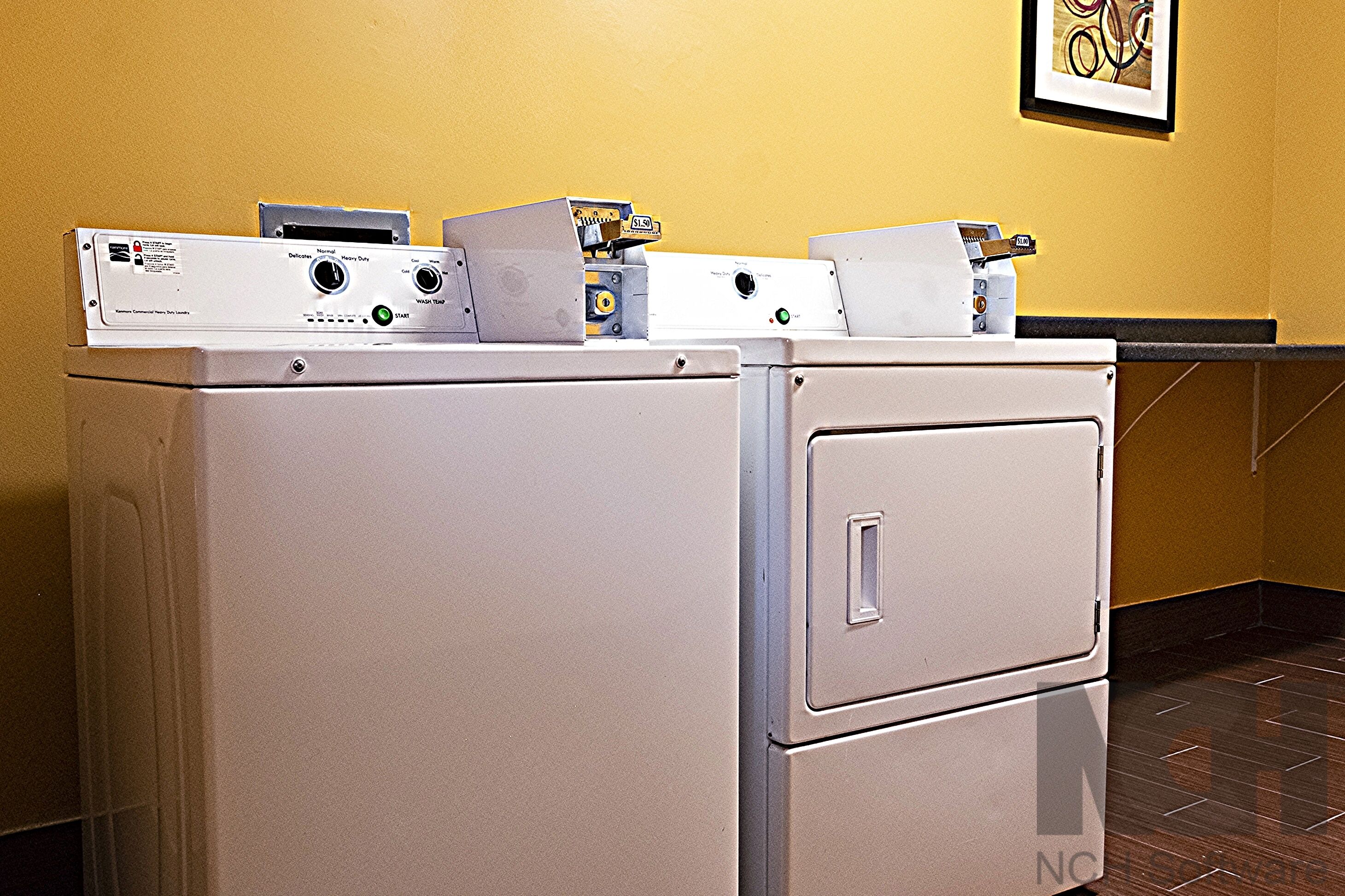 A laundry room with stacked washing machines and dryers, a tiled floor, and a framed artwork on the wall.