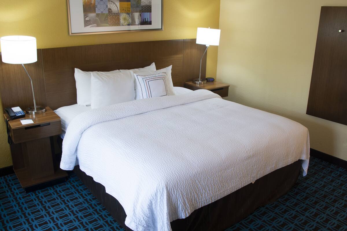 A hotel room with a large bed, two bedside tables with lamps, a telephone, and a framed picture on the wall.