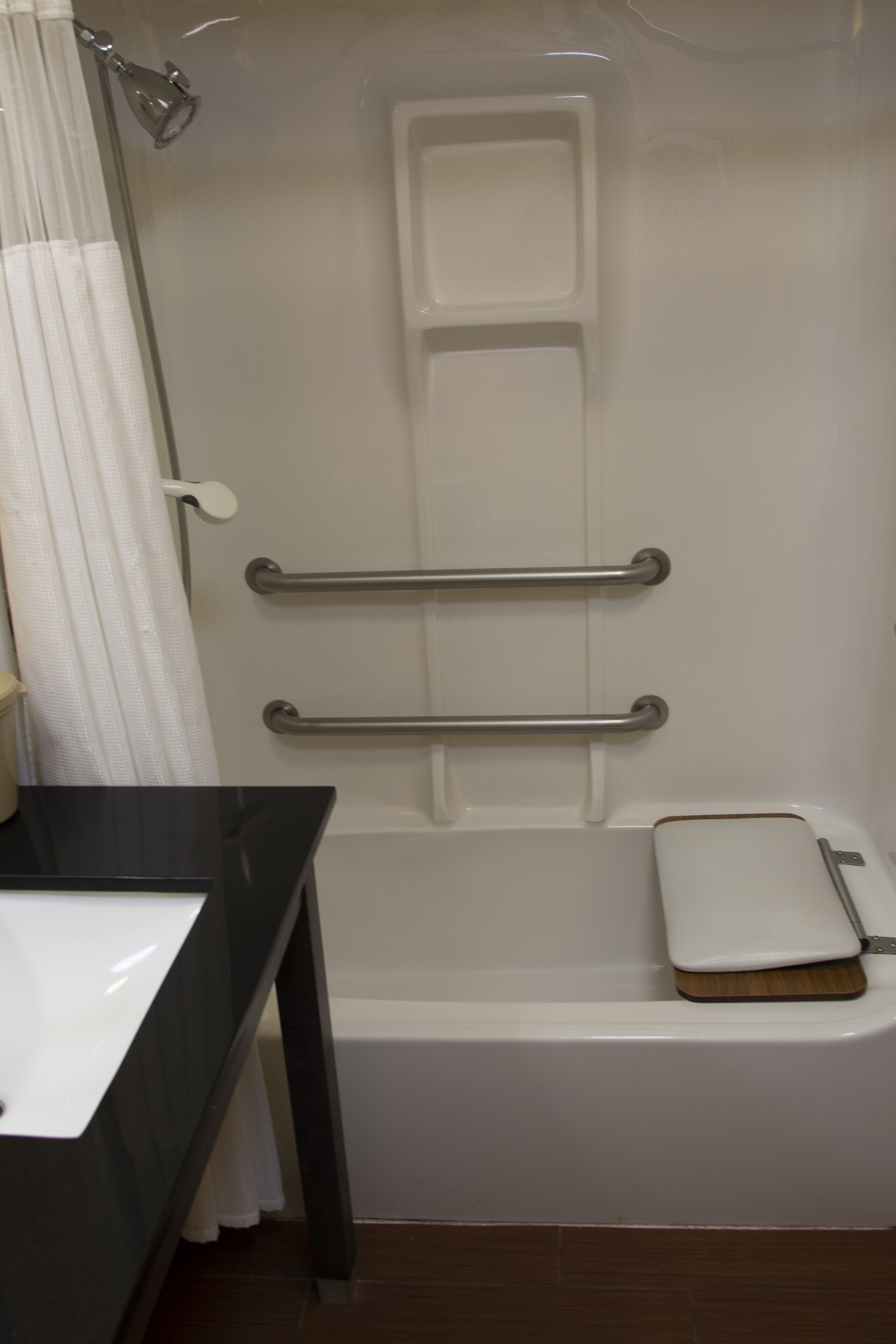 A bathroom with a bathtub, a toilet, and a sink. There are two metal grab bars installed for support.