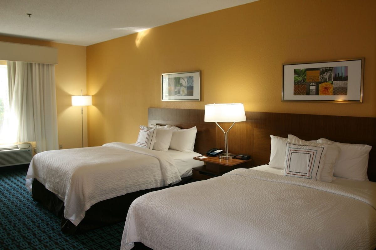 A hotel room with two beds, a nightstand with a lamp, a telephone, and two framed pictures on the wall.