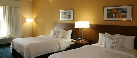 A hotel room with two beds, a nightstand with a lamp, a telephone, and two framed pictures on the wall.