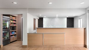 A modern hotel lobby with a wooden reception desk, a refrigerated beverage cooler, and a microwave. - Fairfield by Marriott Inn & Suites Jacksonville (Jacksonville)