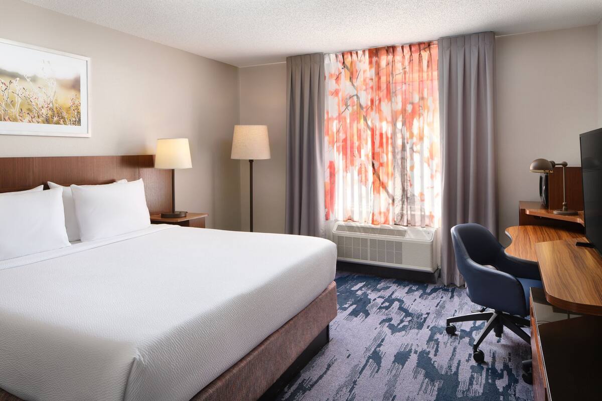A hotel room with a large bed, a desk, a chair, a lamp, and a television.