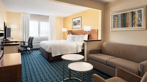 Habitación de hotel con cama, dos mesitas de noche, sofá, escritorio con silla y televisor.