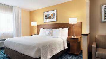 Quarto de hotel com cama grande, duas luminárias de cabeceira, painel de cama e uma cadeira.