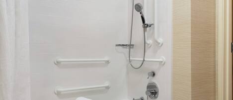 A modern bathroom with a white bathtub, a handheld showerhead, and grab bars.