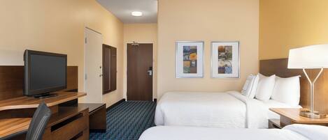 A hotel room with two beds, a desk with a TV, a door, and two framed pictures on the wall.