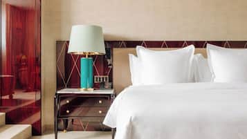 A hotel room with a bed, bedside table, lamp, and a view of a red wall.