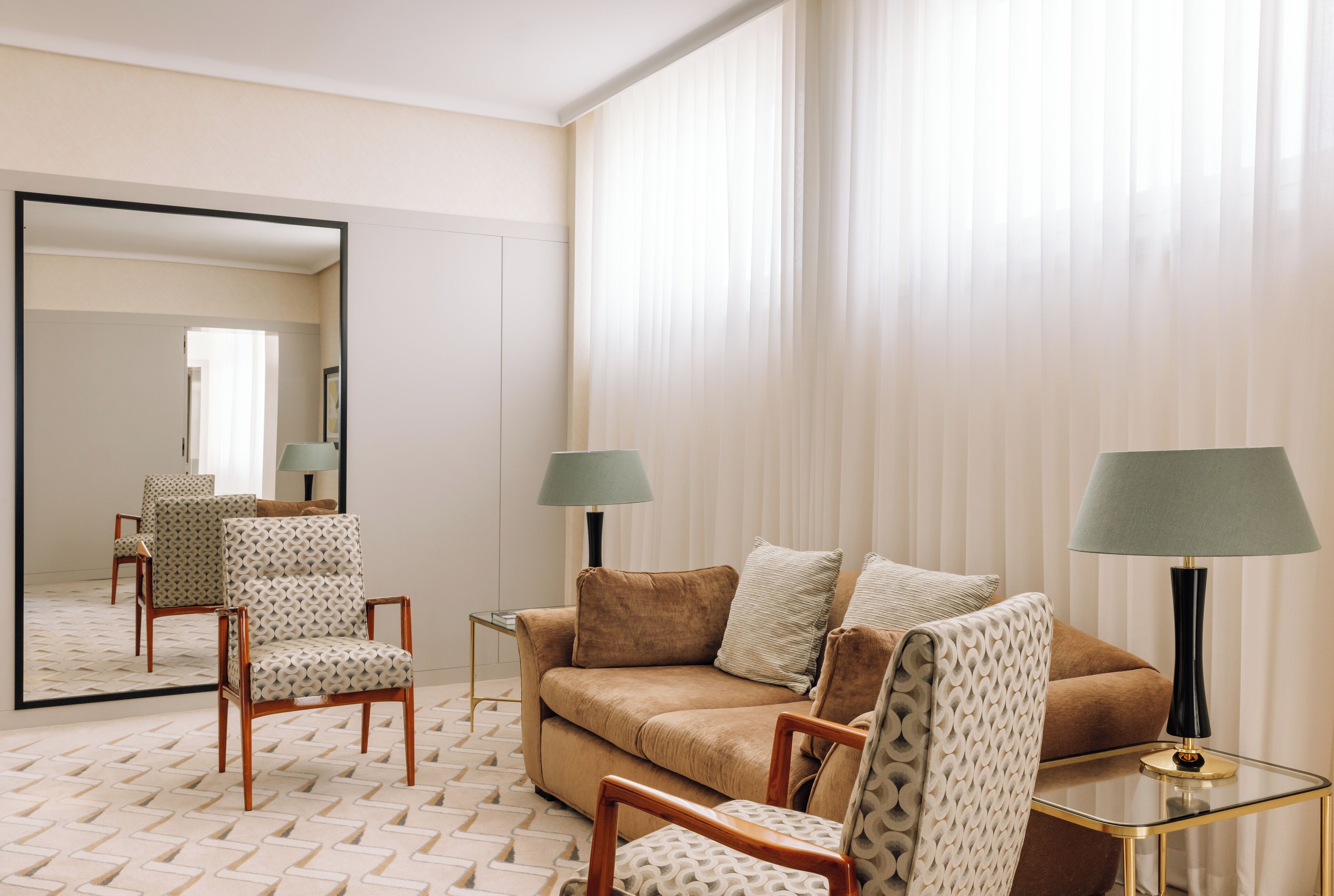 Hotelkamer met een bank, twee fauteuils, een salontafel, een bijzettafeltje en een spiegel.