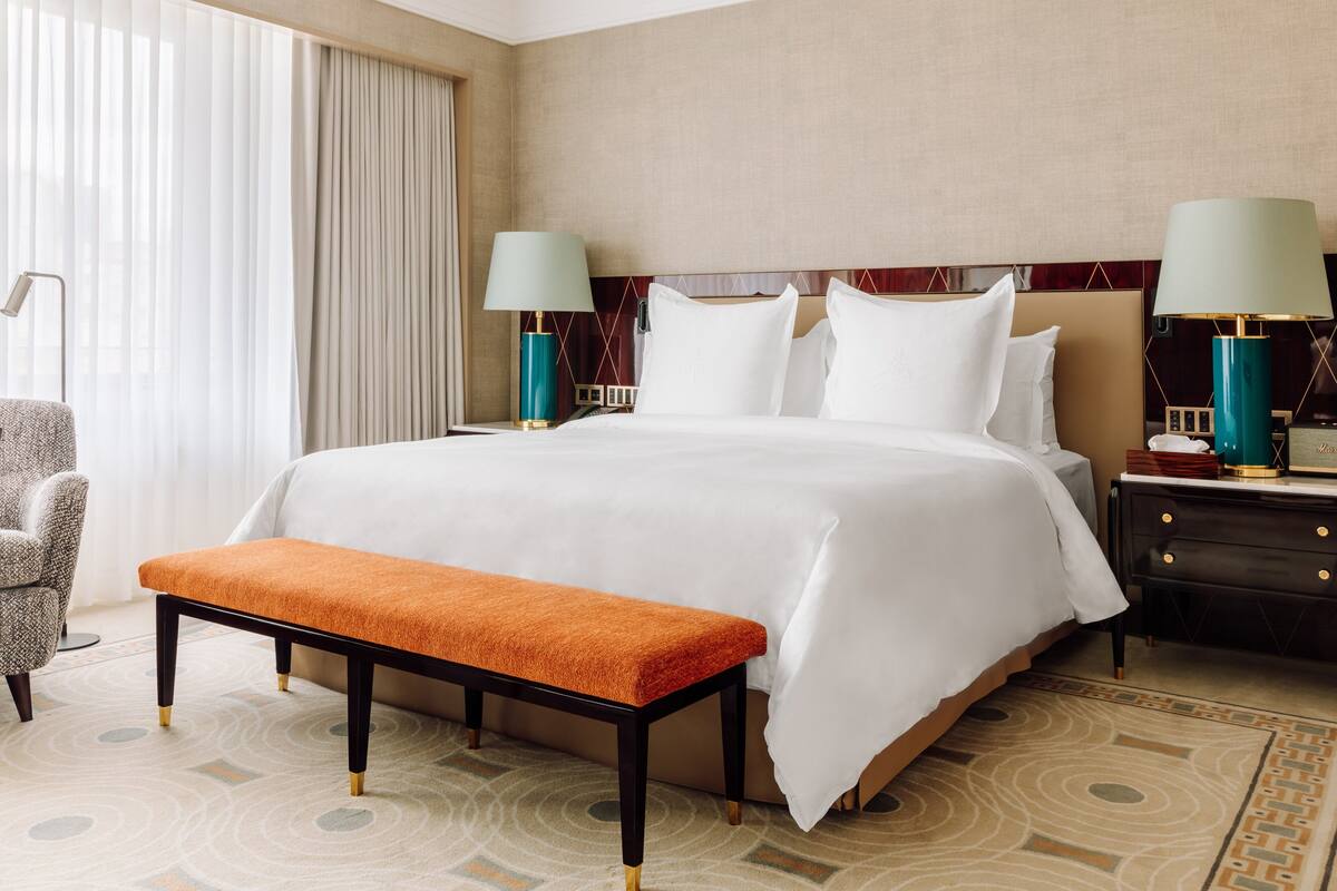 A hotel room with a large bed, two bedside tables with lamps, a bench, and a patterned rug.