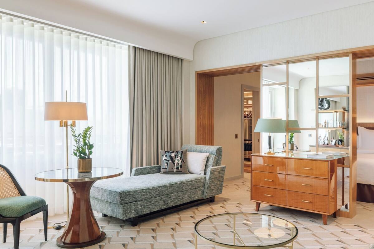 A hotel room with a sofa, a wooden dresser, a round glass table, a lamp, and a large mirror.