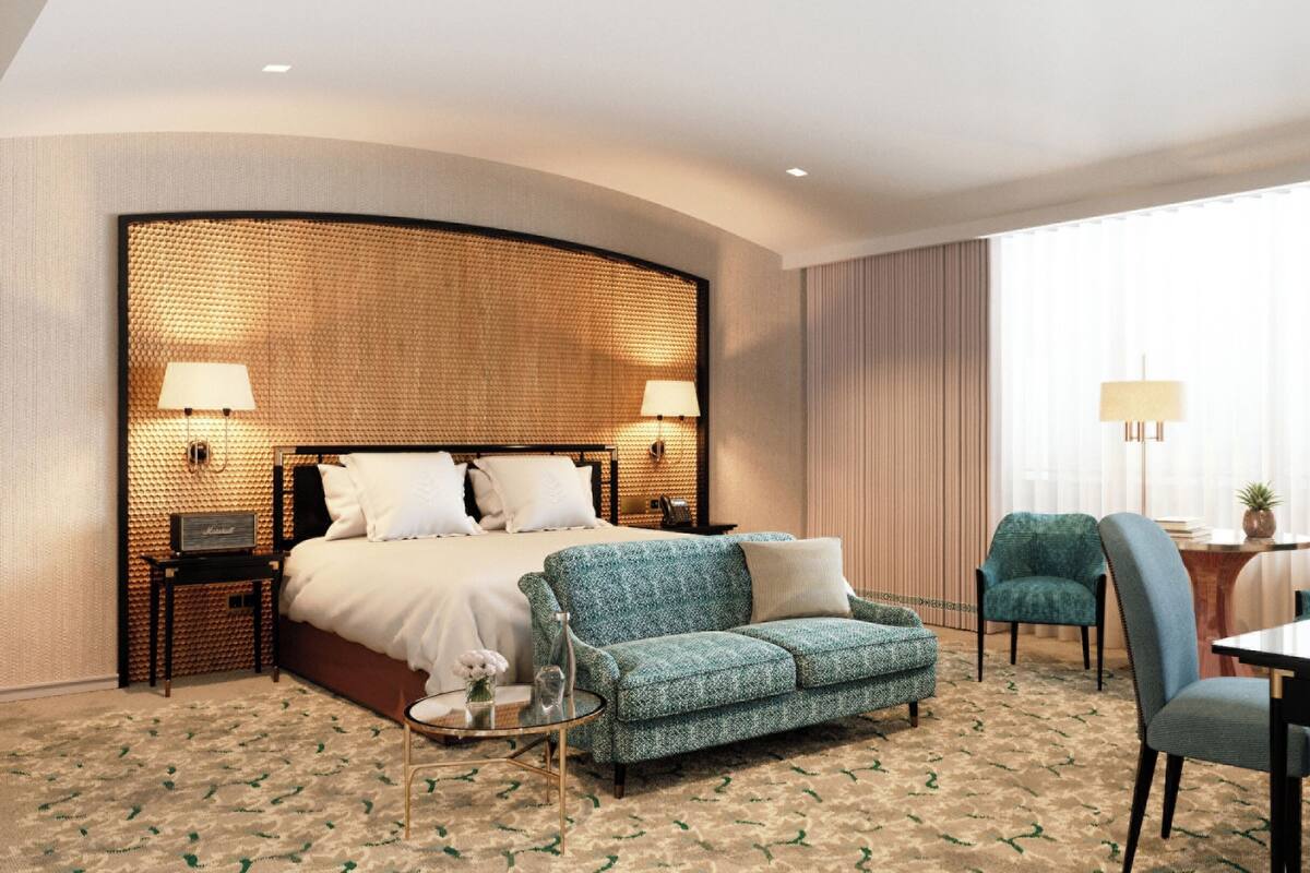 A hotel room with a large bed, a sofa, a dining table, and two chairs. There are lamps on the bedside table and a lamp on the dining table.