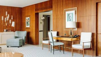 Habitación de hotel con pared de paneles de madera, un escritorio con teléfono, dos sillas, una lámpara y un cuadro enmarcado.