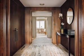 A hallway with wooden walls, a carpeted floor, a dining area in the background, and a mirror on the right.