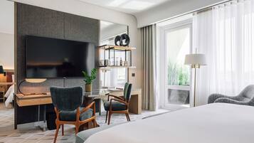 Una habitación de hotel moderna con una cama grande, un escritorio con computadora, un televisor de pantalla plana y una zona de estar con sillas.