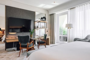 A modern hotel room with a large bed, a desk with a computer, a flat-screen TV, and a seating area with chairs.