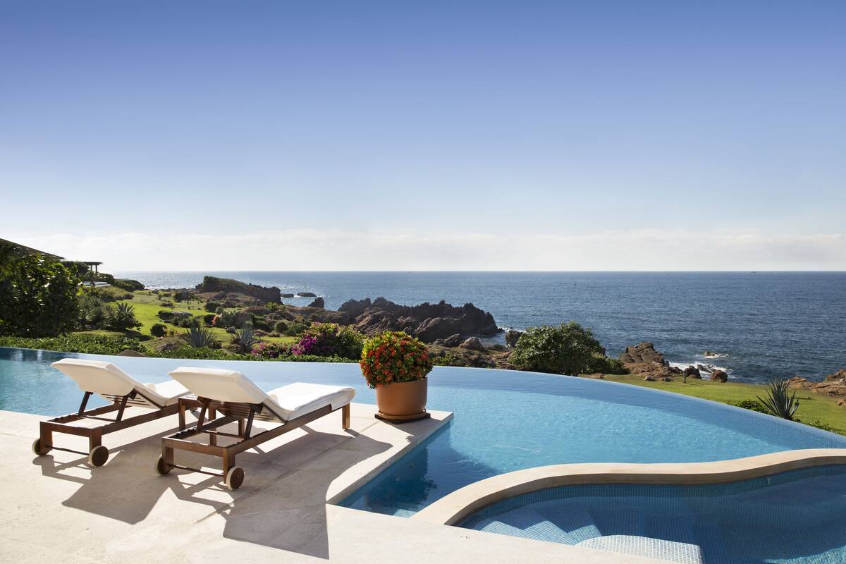 Una piscina infinitum amb gandules i una planta en test, amb vistes a una costa rocosa i l'oceà.