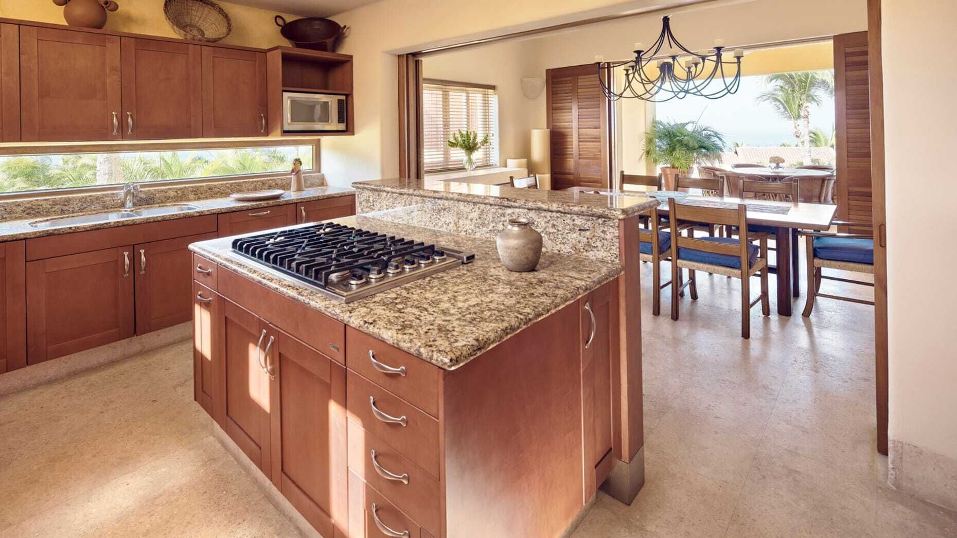 Una cocina con encimeras de granito, gabinetes de madera, estufa integrada y un comedor con mesa y sillas.