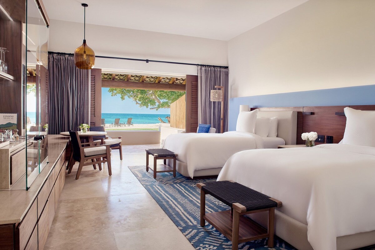 Habitación de hotel con dos camas, un escritorio y vistas a la playa.