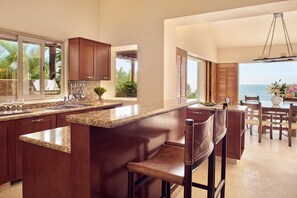 A modern kitchen with a large island, wooden cabinets, and a view of the ocean.