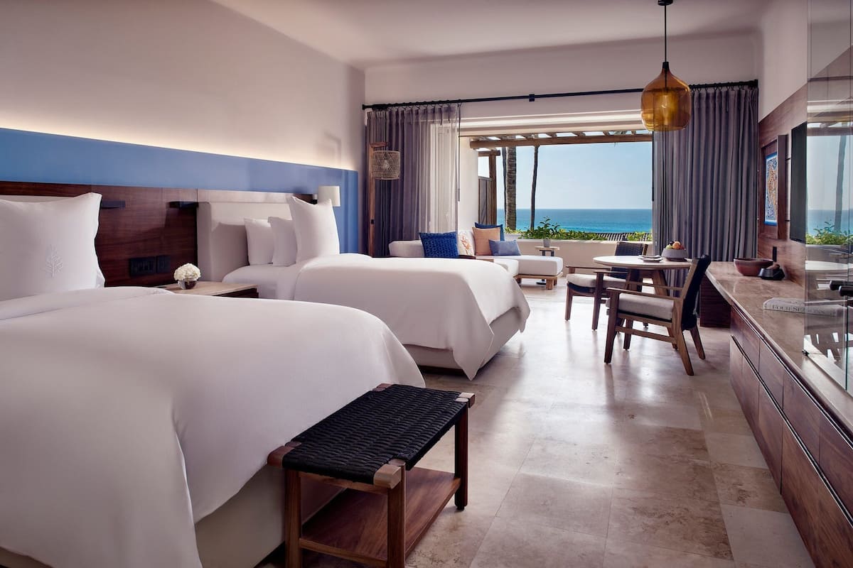 Habitació d'hotel amb dos llits, una petita zona de dinar, una banca i vista a l'oceà.