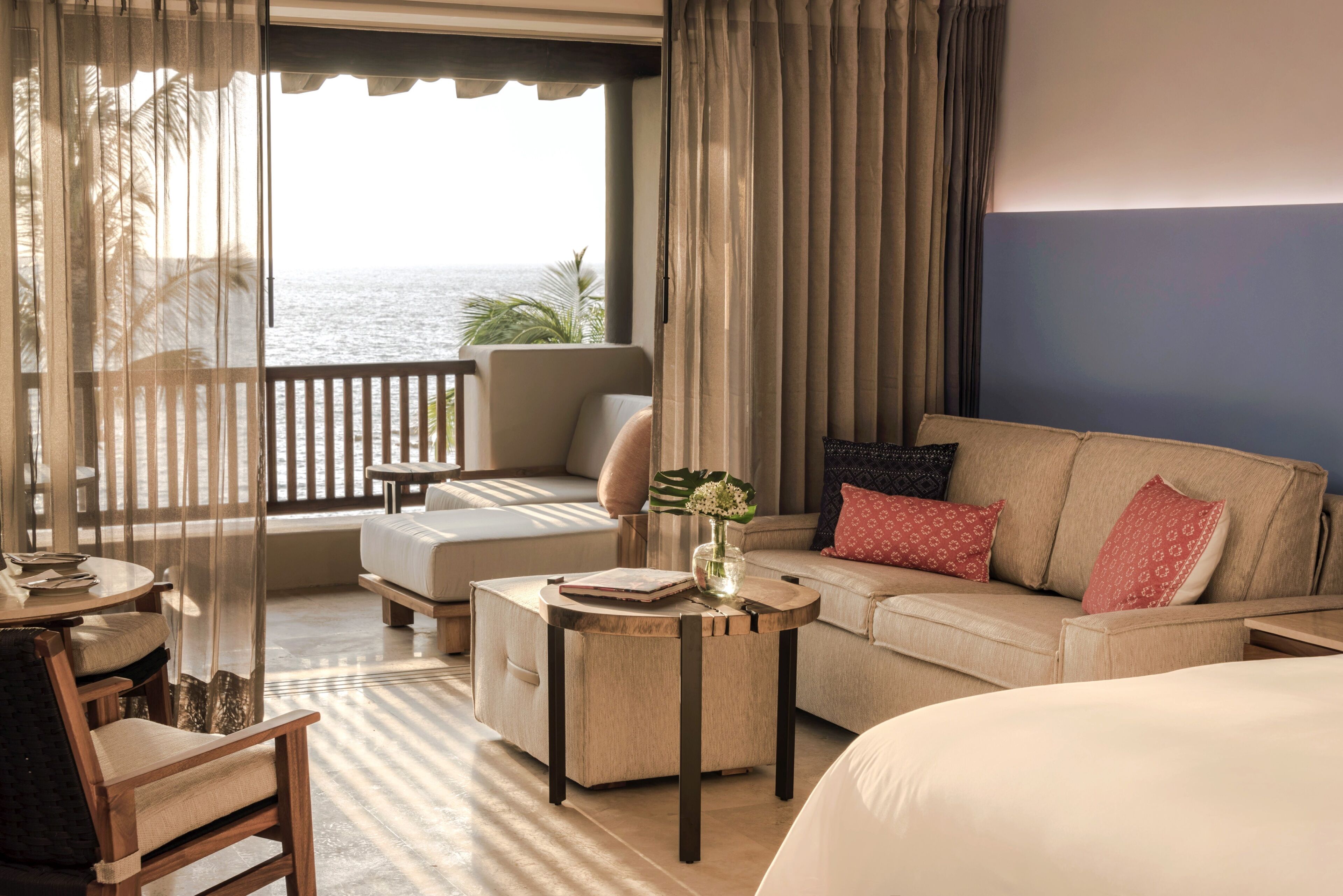 Een hotelkamer met balkon, een bank, een bed en een kleine tafel met een bloevas.