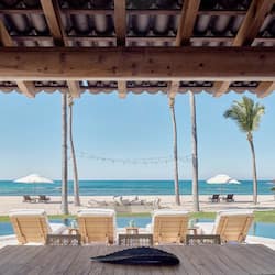 Relax in a serene outdoor space with lounge chairs and a table overlooking the ocean and palm trees.
