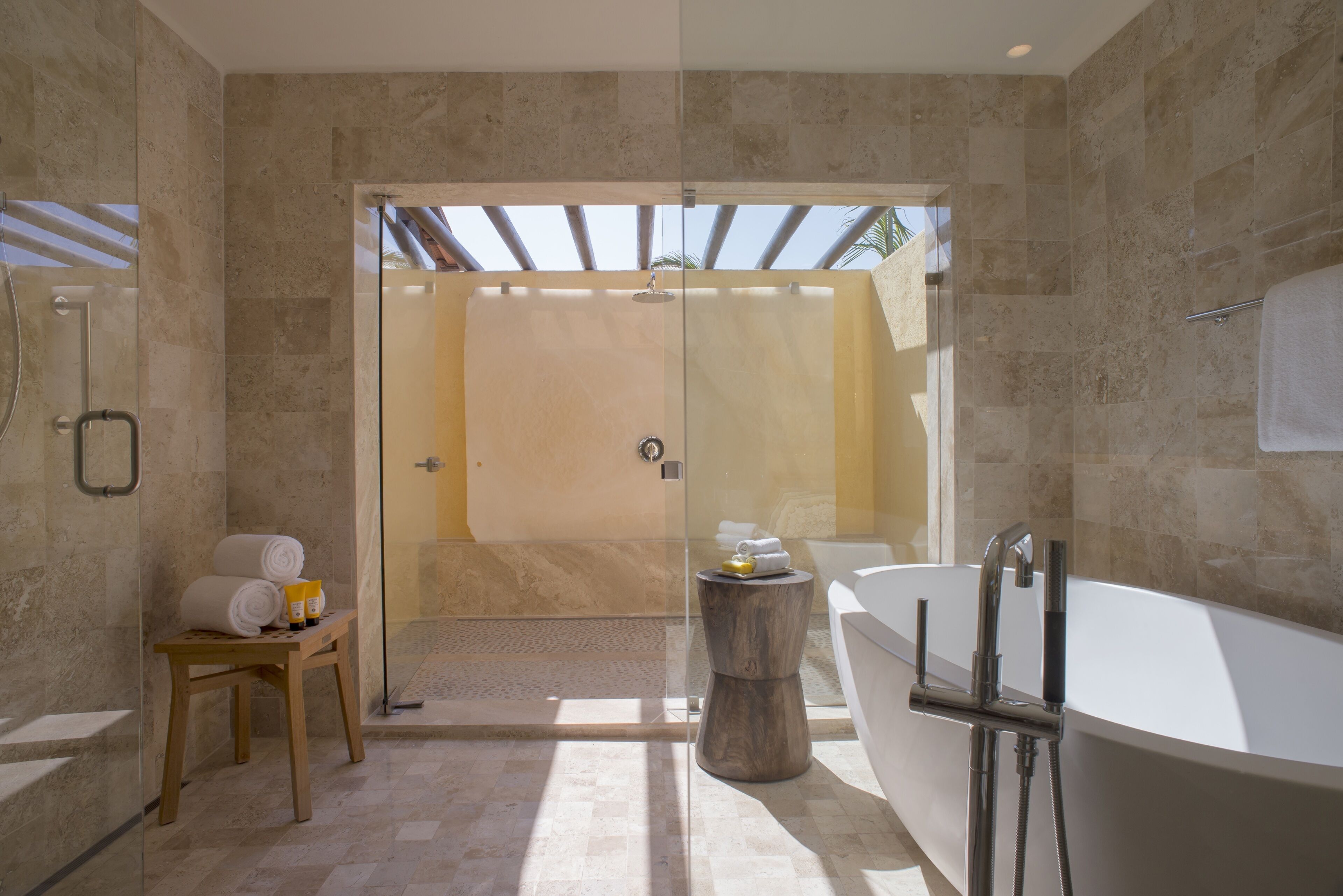 Une salle de bain moderne avec une douche à parois de verre, un tabouret en bois sur lequel sont posées des serviettes et une baignoire sur pieds.