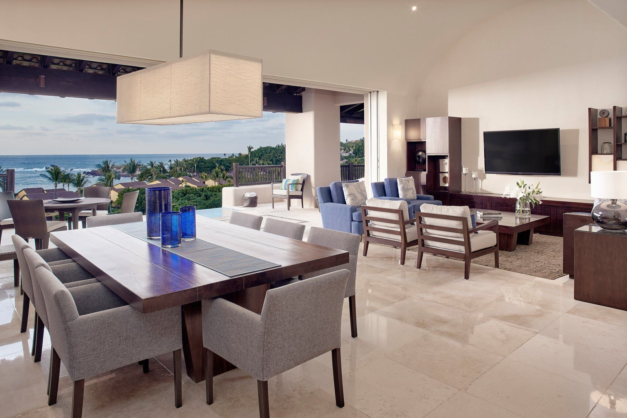 A spacious living area with a large dining table, comfortable seating, a flat-screen TV, and a view of the ocean.