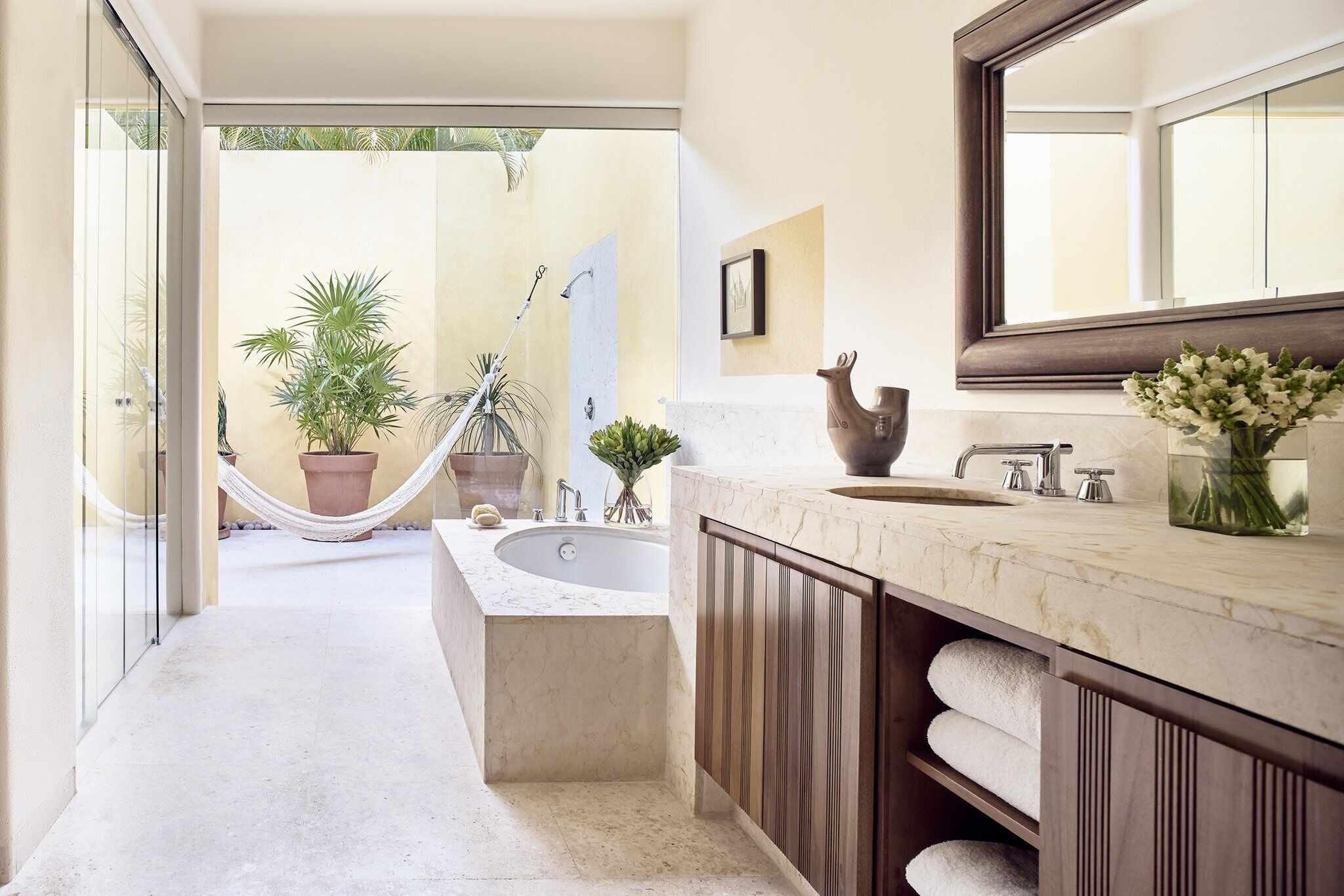 Un baño moderno con un lavamanos grande, una bañera y una ducha. Se ve una planta en maceta y una hamaca al fondo.