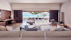 Un moderno salón con vista a la playa, un ventilador de techo y una zona de comedor con mobiliario de exterior.