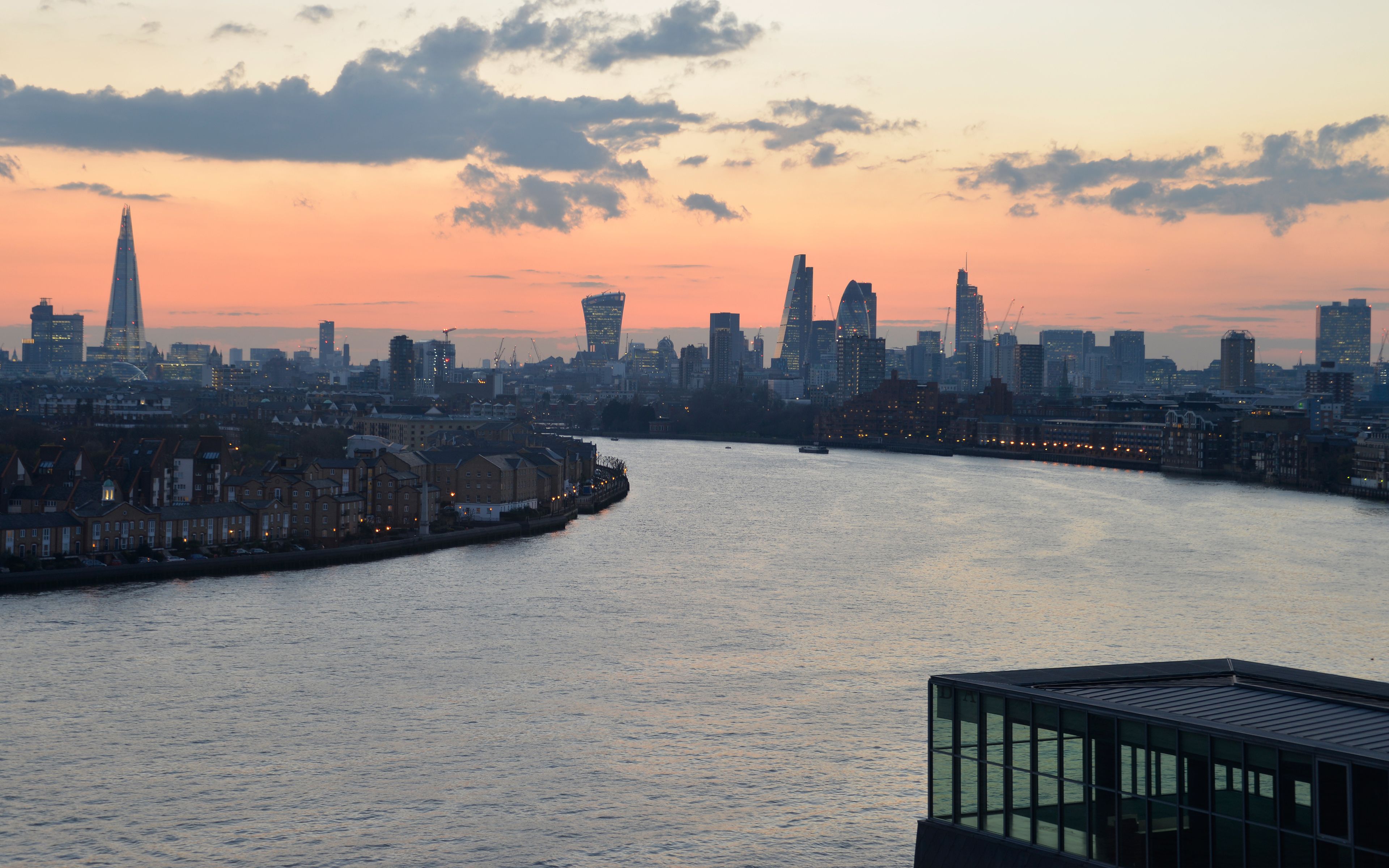 A city skyline at sunset with a river in the foreground.