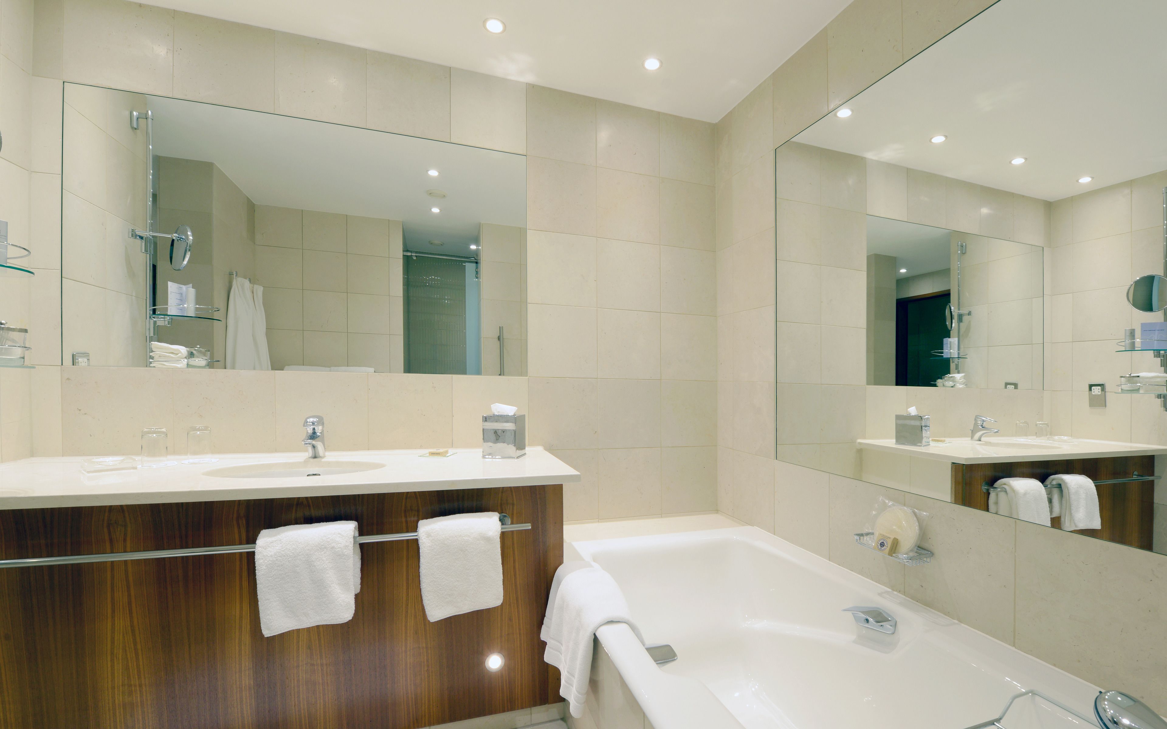 A modern bathroom with two sinks, a bathtub, and large mirrors.