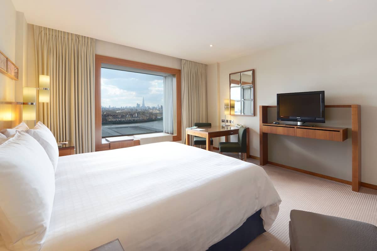 A hotel room with a large bed, a desk, a television, and a view of a cityscape.