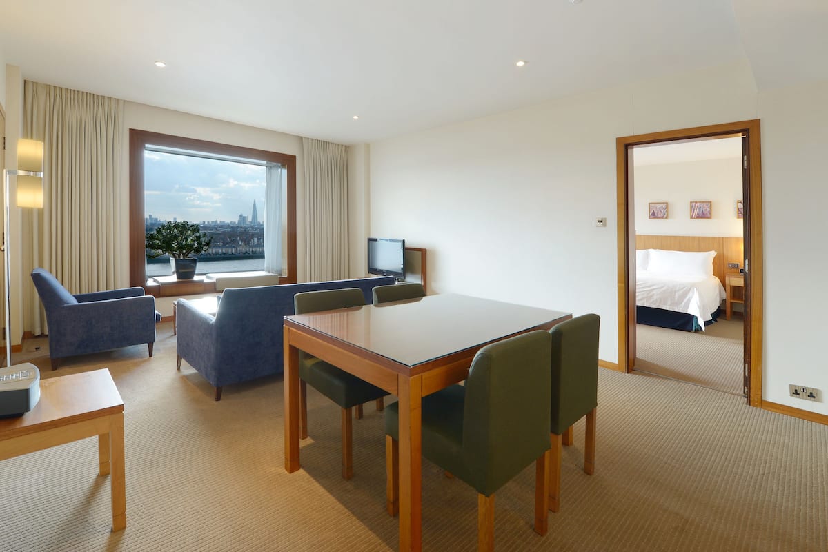 A hotel room with a large window, a dining area, a TV, and a bed.
