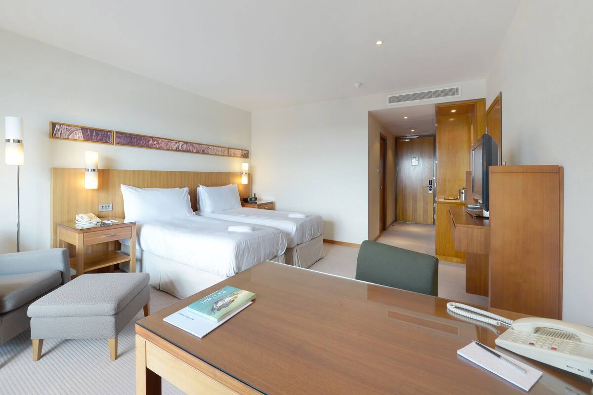 A hotel room with a bed, bedside tables, a desk, a chair, a telephone, and a television.