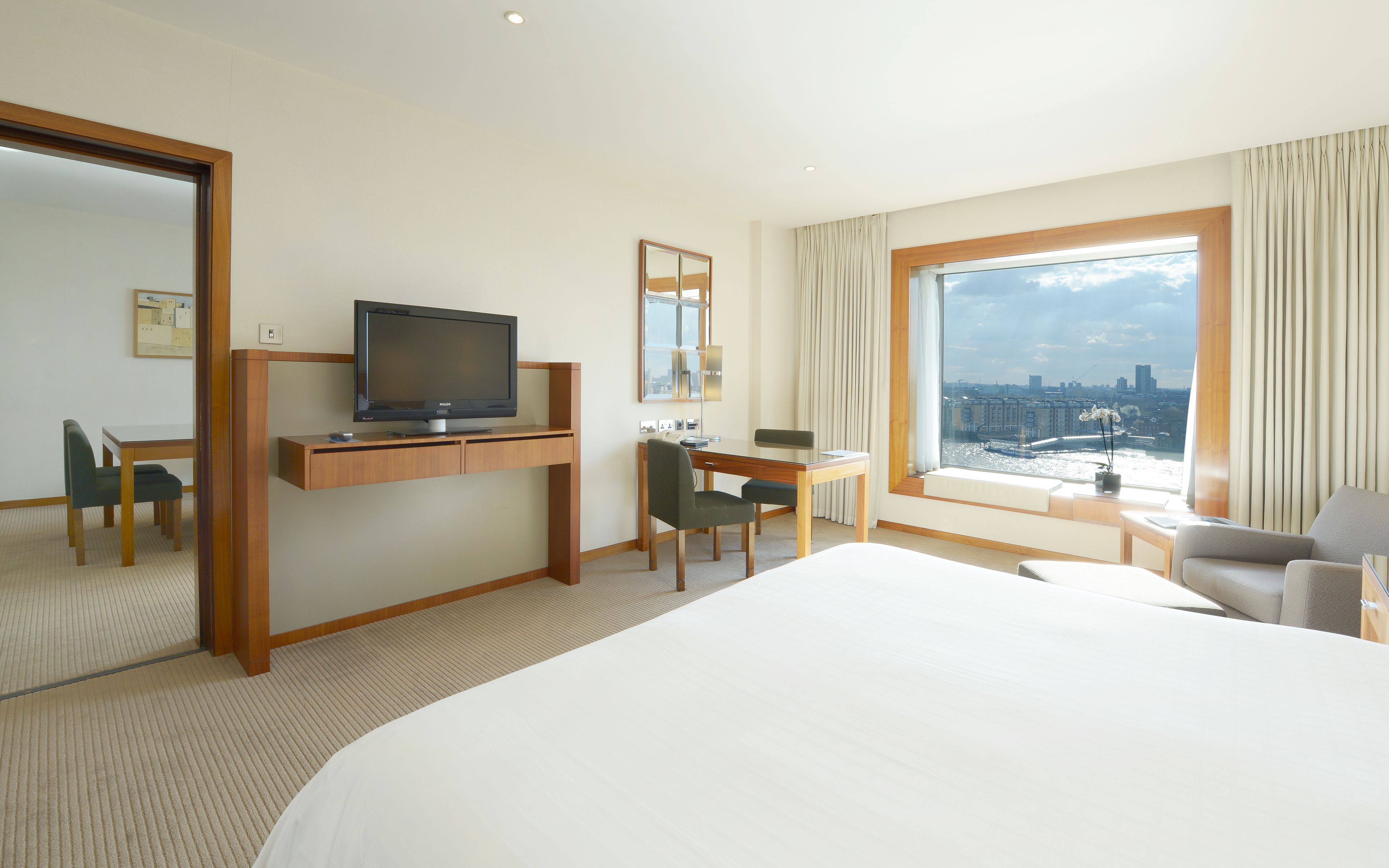 Una habitación de hotel con una cama, un escritorio con televisor, una silla, una mesa de comedor y un ventanal con vistas a la ciudad.