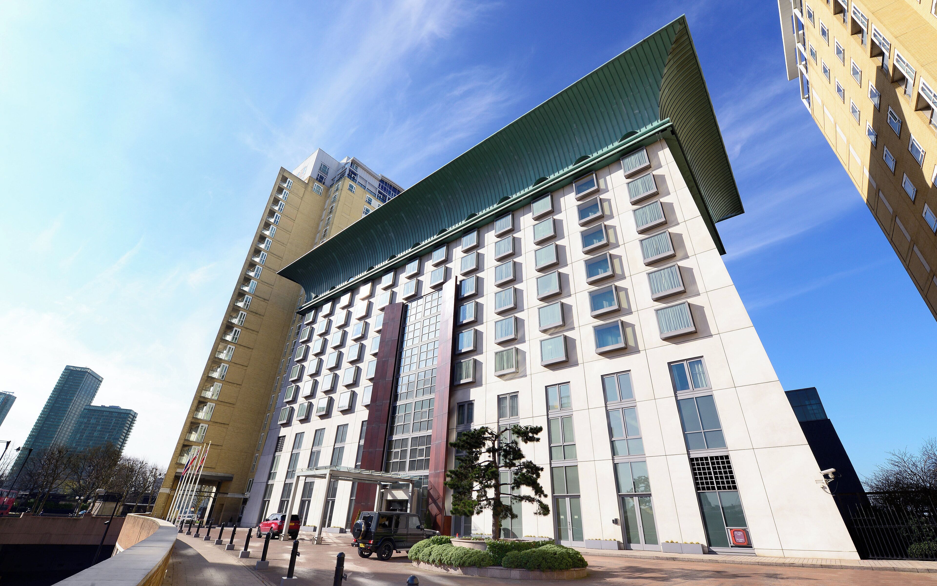 A modern hotel with a prominent green roof, multiple floors, and a central entrance.