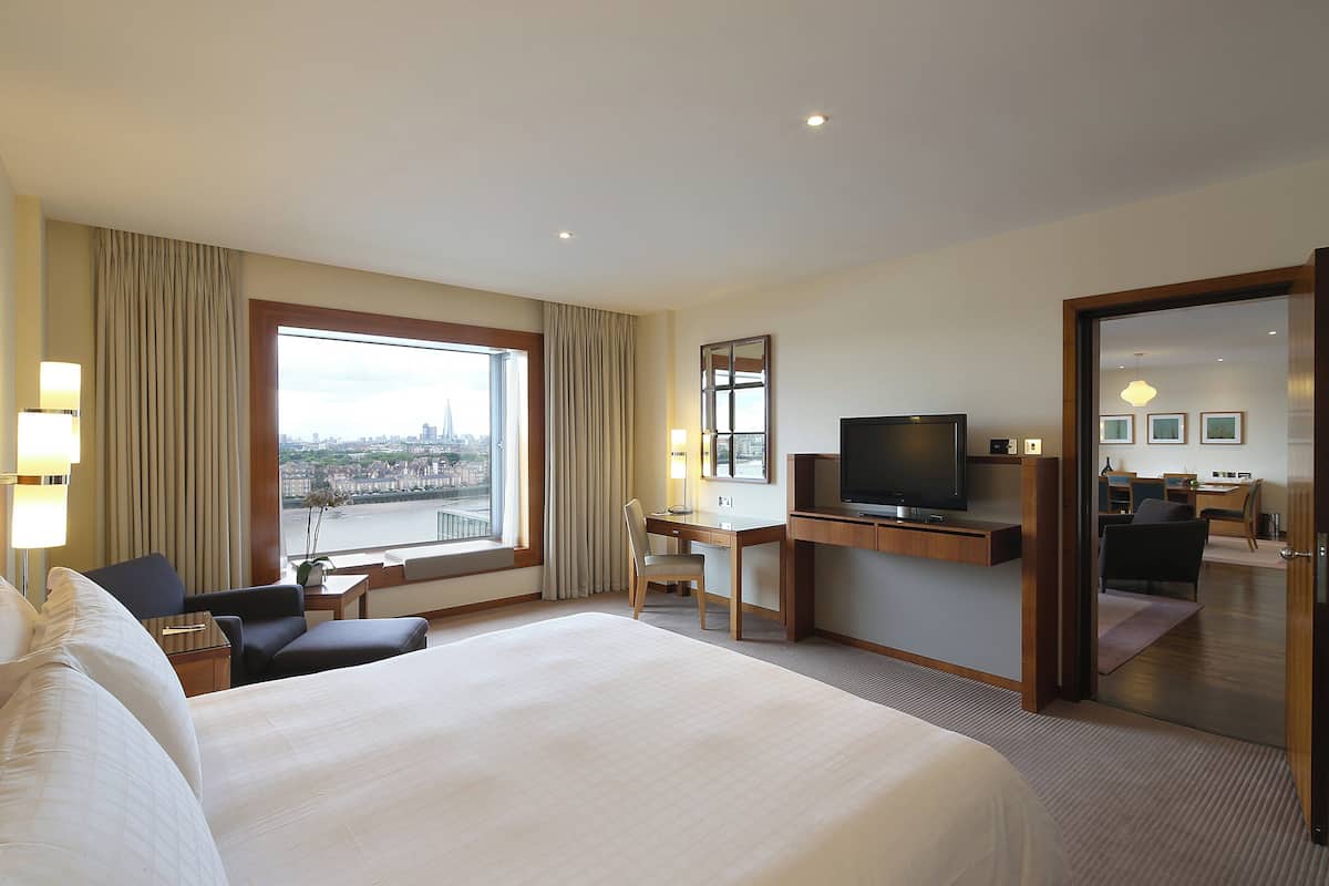 A hotel room with a large bed, a desk with a chair, a television, and a view of the city through the window.
