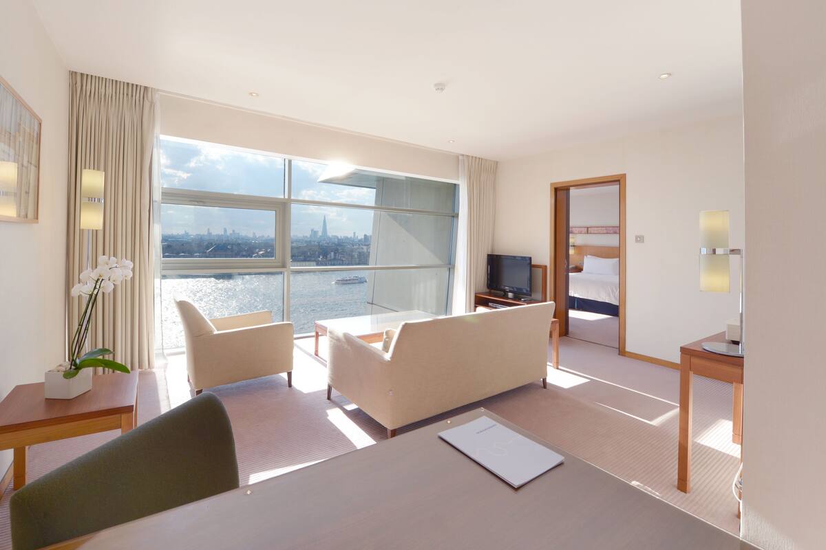 A hotel room with a large window, a bed, a TV, a desk, and a chair.